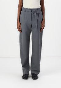 Pantalon gris avec une coupe droite, la texture du tissu est lisse. Il dispose d'une taille avec un bouton et d'un détail de lien en tissu.