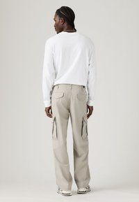 Biela košeľa s dlhým rukávom skombinovaná s svetlo béžovými cargo nohavicami s bočnými vreckami, vo voľnom strihu a rovnom strihu nohavíc.
