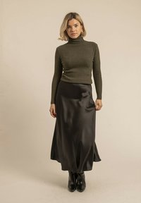 Pull encolure haute à côtes olive associé à une longue jupe fluide en satin noir, complété par des bottes noires montantes.