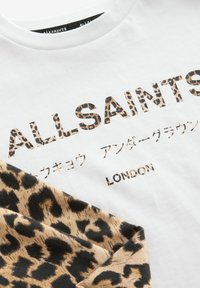Biała koszulka z akcentami w panterkę oraz logo „ALLSAINTS” w brązowym i czarnym napisie. Wykonana z miękkiej bawełny, w fasonie z okrągłym dekoltem.