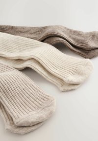 Drei Paar gerippte Stricksocken in Beige, Creme und Hellbraun liegen flach auf einer weißen Oberfläche.