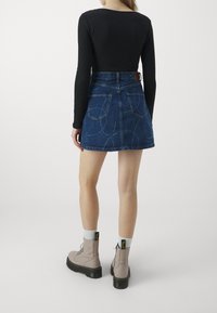 Jeanskjol med figursydd midja, blå färg och två bakfickor. Kombinerad med en svart långärmad topp och beige snörstövlar.