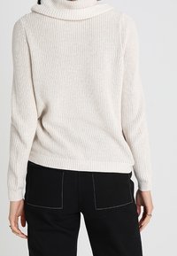 Cremefarbener Strickpullover mit hohem Rollkragen, geripptem Saum und Bündchen, mit lockerem Sitz und strukturierter Stoffoberfläche. Rückansicht.