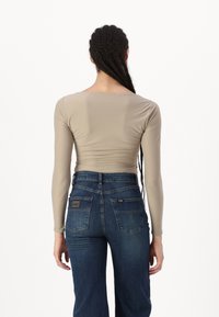 Langärmliges, eng anliegendes beiges Oberteil mit rundem Ausschnitt, kombiniert mit blauen High-Waist-Jeans mit einem Logo-Patch und zwei Gesäßtaschen.