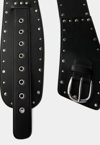 Sort læderbælte med sølv metalnitter og øjer, med en pigbuckle og tekstureret finish. Flad design med justerbar længde.