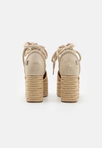 Beige espadrille hakken met geweven touwplatform, stoffen bovenwerk en vetersluiting. Rond toe en merkaccent op de hak.