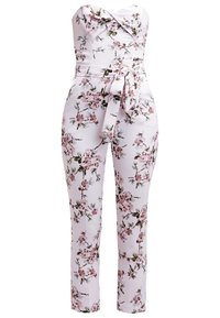 Combinaison florale en tissu rose clair, design sans bretelles, présentant un corsage froncé et une ceinture nouée à la taille. Motif floral dans des nuances de rose et de vert.