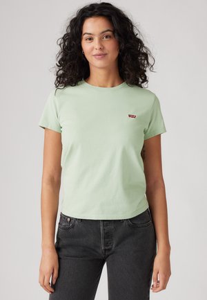T-shirt en coton vert clair avec des manches courtes, un col rond et un petit logo rouge Levi's sur la poitrine gauche. Porté avec un jean noir.