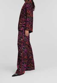 Costume à motif floral en tissu sombre, avec des nuances de rose et d'orange. Veste avec revers et manches longues, associée à un pantalon à jambes larges.