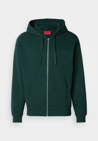 Grøn zip-up hættetrøje med en kængurulomme, snøre i hætten og ribbede manchetter. Har et lille logo på venstre brystområde. Blødt stoftekstur.