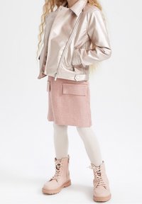 Chaqueta de cuero sintético rosa metálico con cierre de cremallera, combinada con una falda rosa texturizada que presenta dos bolsillos frontales y botas rosa claro con cordones.