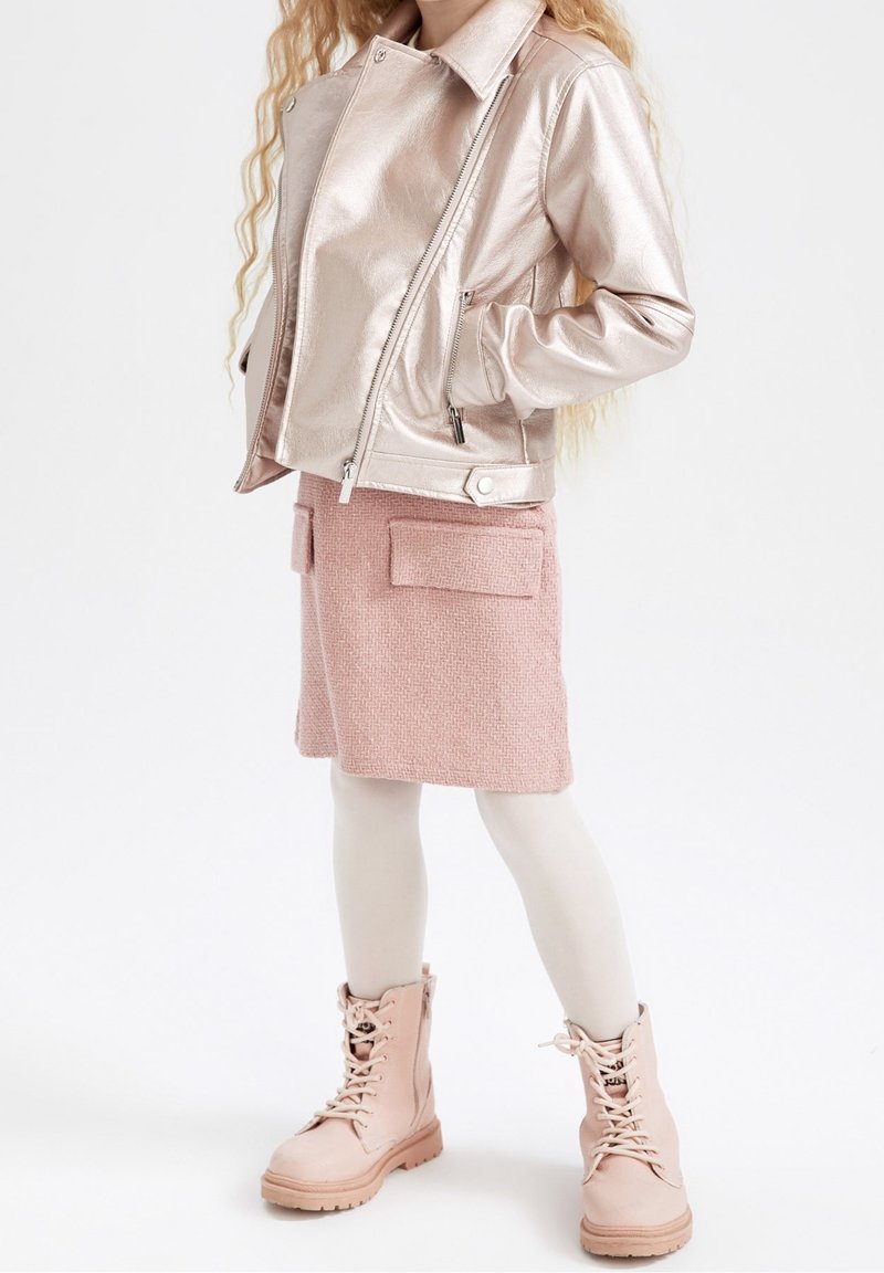 Metallic-rosafarbene Kunstlederjacke mit Reißverschluss, kombiniert mit einem texturierten rosa Rock mit zwei Fronttaschen und hellrosa Schnürstiefeln.