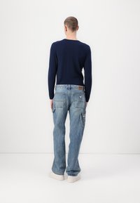 Marineblå skjorte med lange ærmer parret med lyseblå denim cargo-bukser, der har flere lommer og et lædermærkeskilt på livet.
