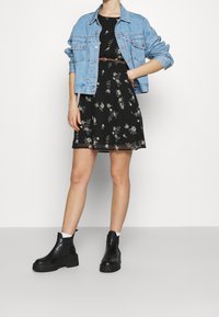 Kukkakuvioinen musta mekko, jossa on kapea vyötärö ja liehuva hame, päällä vaalea sininen farkkutakki. Mustat paksut nilkkurit valkoisten sukkien kanssa.