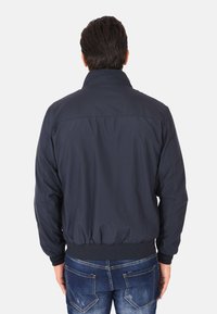 Giubbotto bomber blu navy con colletto alto, vita e polsini elasticizzati. Tessuto liscio con vestibilità comoda, visto da dietro.