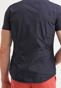 Kortärmad skjorta i mörk marinblått tyg, med en slät yta, skräddarsydd passform och subtil sömdetaljering längs ryggen.