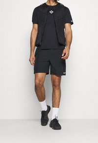 Schwarzes Sportoutfit mit einer gesteppte Weste, kurzen Ärmeln und Shorts; alle Teile in einheitlichem Schwarz mit dezentem Branding und Shorts über dem Knie.