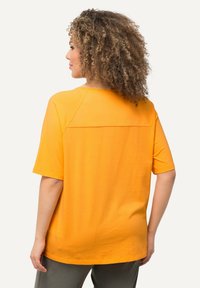 T-shirt arancione a maniche corte con un fit rilassato. Presenta un design con spalla raglan e una texture di cotone liscia. Il retro ha un dettaglio di cucitura orizzontale.
