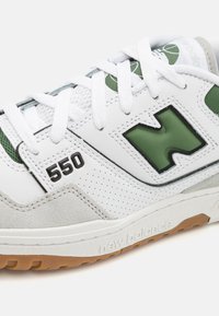 Vita sneaker med gröna accenter, material av mocka och läder, perforerat mönster, '550' i svart och sula av gummigummi med texturerat mönster.