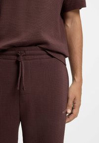 Burgunderrotes, geripptes Baumwoll-Loungewear-Set mit Kurzarmshirt und Kordelzughose mit dezentem Logodetail. Strukturierte Oberfläche.