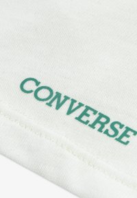 Λευκό βαμβακερό ύφασμα με υφή, με την επιγραφή "CONVERSE" σε τιρκουάζ. Η σχεδίαση περιλαμβάνει ραμμένο τελείωμα.
