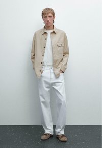 Lys beige skjorte med knapper og en brystlomme, parret med hvide bukser og brune loafers. Enkel, afslappet pasform, tekstureret stof.