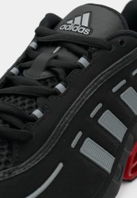 Crna sportska cipela sa teksturiranim gornjim dijelom, sivim detaljima i prepoznatljivim crvenim potplatom. Reflektirajući elementi poboljšavaju vidljivost.