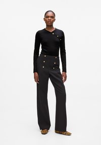 Top nero a maniche lunghe con design avvolgente e dettagli in bottone dorato abbinato a pantaloni neri a vita alta e gamba larga con accenti dorati.