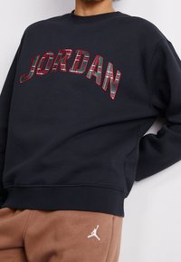 Felpa nera con "JORDAN" in un design a quadri rosso e verde. Tessuto morbido, collo a giro e polsini a costine. Jogger marroni con logo.