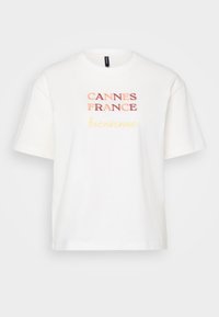 Hvit bomull T-skjorte, kort erm, med "CANNES FRANCE" i rødt og "Bienvenue" i gult, med rund hals.