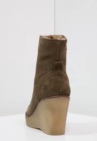 Stivaletto con zeppa in camoscio marrone, punta arrotondata, tomaia texturizzata e suola in gomma. Presenta un piccolo logo vicino al tallone e una chiusura con cerniera.