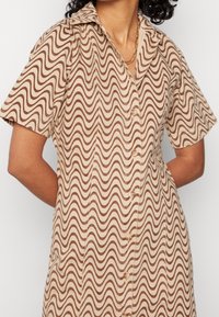 Robe à manches courtes marron et beige avec un motif en vagues, un col classique et une fermeture à boutons à l'avant. Tissu léger à texture lisse.