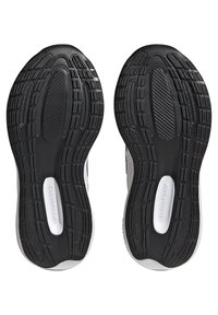 Las suelas de zapatos de goma negra presentan un patrón de textura con estrías y surcos. Las suelas incluyen una etiqueta blanca con la palabra "CLOUDFOAM".