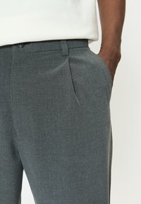 Sivé na mieru šité nohavice s jemnou textúrou, prednými záhybmi a bočnými vreckami, vyrobené z ľahkej tkaniny, kombinované s bielou košeľou.