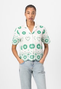 Korte mouw shirt met een witte basis versierd met groene bloemen- en hartpatronen, een golvende zoom en een borstzakje.