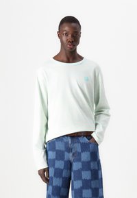 Light mint long-sleeve shirt with subtle stripes and a small graphic, paired with blue patterned denim pants. Material appears soft.