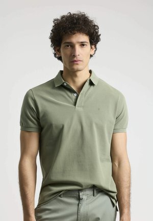 Polo en color verde oliva con mangas cortas, textura de algodón suave, tapeta de tres botones y un pequeño logo en el lado izquierdo del pecho.