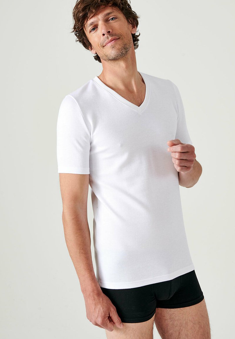 Witte V-hals T-shirt gemaakt van soepel katoen, korte mouwen, aansluitend ontwerp, gedragen met zwarte boxers; model staat met een ontspannen houding.
