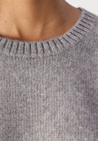 Suéter gris de punto con un cuello redondeado acanalado. La tela parece suave con un acabado texturizado y sutiles variaciones en el tono.