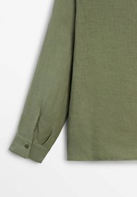 Manche longue d'une chemise en lin vert olive avec poignet boutonné, texture visible et plis subtils.