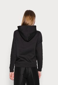 Felpa nera con tasca a marsupio, polsini a costine e un ampio cappuccio. Il tessuto sembra morbido con una texture liscia.