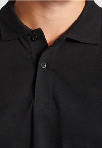 Black polo shirt with a textured fabric. Features a collar and two button placket, showcasing a simple and classic design.