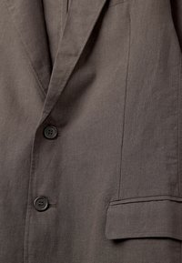 Grauer Leinenblazer mit Reverskragen, zwei schwarzen Knöpfen und einer einzigen Brusttasche mit dezenten Nähdetails.