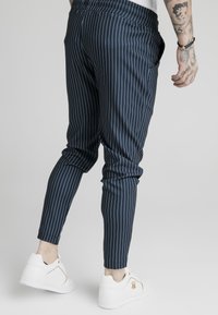 Marinrandiga avsmalnande byxor med elastisk midja och sidofickor, ihop med vita sneakers med gulddetaljer.