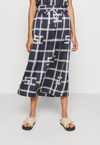 Jupe midi marine avec un motif à carreaux blancs et des accents de logo. Elle dispose d'une taille élastique avec cordon de serrage, d'un tissu léger et d'une coupe fluide.