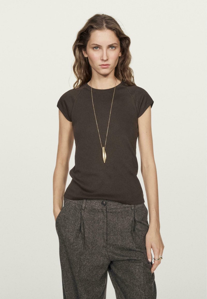 T-shirt fitted marrone scuro con maniche a cappuccio, abbinato a pantaloni grigi su misura e testurizzati, con una collana con pendente dorato.