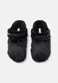 Μαύρα φουντωτά ξύλινα υποδήματα με μαλακή υφή, στρογγυλό σχήμα, ανοιχτή πλάτη και ορατό λογότυπο στη ζώνη. Κατάλληλα για εσωτερική χρήση.