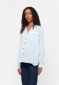 Light blue button-up shirt with vertical white stripes, two chest pockets, and gold buttons. Long sleeves with buttoned cuffs.