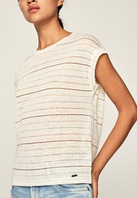 Koszulka w paski w jasnym kremowym kolorze, z cienkimi poziomymi liniami w kolorze czerwonym i zielonym, o luźnym kroju i podwiniętych krótkich rękawach. Gładka faktura.