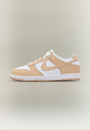 Niski model sneakersów Nike z białymi i beżowymi panelami ze skóry, białymi sznurówkami oraz gumową podeszwą na neutralnym tle.